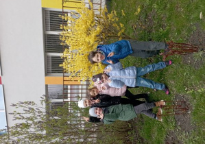 Dzieci pozują do zdjęcia przed kwitnącym krzewem forsycji